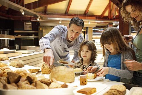 Ein Mann und zwei Kinder stehen um einen Tisch mit Essen. in der Unterkunft Center Parcs Heijderbos Limburg-Weeze in Heijen