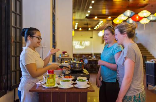 eine Gruppe von Frauen steht um einen Tisch mit Essen herum in der Unterkunft Hoi An Hai Au Boutique Hotel in Hoi An