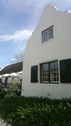 a white house with black windows and green shutters at De Kloof Heritage Estate and Wellness in Swellendam