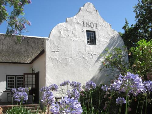 a white building with a window and purple flowers at De Kloof Heritage Estate and Wellness in Swellendam