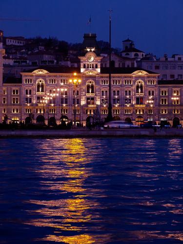a building lit up at night next to the water at Residence Theresia- Tailor Made Stay in Trieste