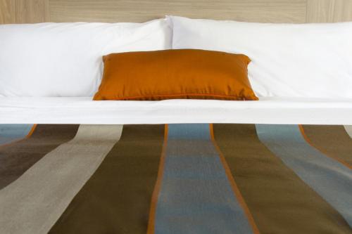a white bed with an orange pillow on it at Wingate by Wyndham Dieppe Moncton in Moncton
