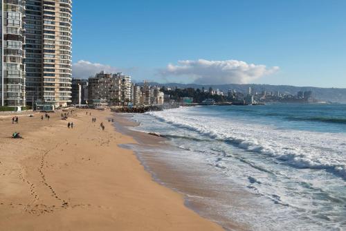 a beach with people walking on the sand and the ocean at Pullman Vina del Mar San Martin in Viña del Mar