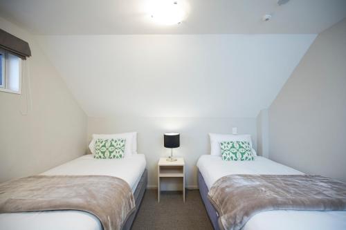 2 Betten in einem Zimmer mit einem Tisch und einer Lampe in der Unterkunft Vita Nova Motel in Christchurch