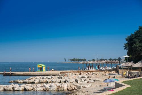 a beach with people and umbrellas and the water at Camping Park Umag Mobile Homes in Umag