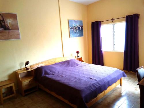 a bedroom with a bed with a purple comforter and a window at Hotel Chez Fanny in Palimé