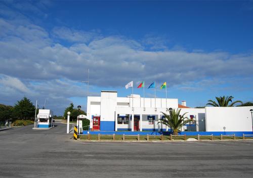 a gas station with flags in a parking lot at Parque de Campismo Orbitur Sitava Milfontes in Vila Nova de Milfontes