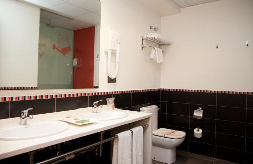 a bathroom with two sinks and a toilet and a mirror at Hotel Bed4U Tudela in Tudela