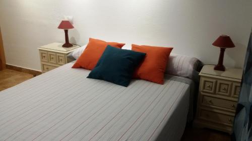 Apartamento de Silvia في أليكانتي: غرفة نوم مع سرير مع وسائد برتقالية وزرقاء