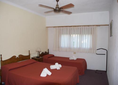 a bedroom with two beds with red sheets and a ceiling fan at Hotel Los Historicos in Villa Gesell