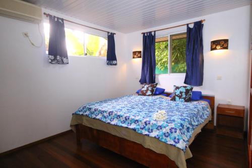 a bedroom with a bed and two windows with blue curtains at Fare Kahaia in Fare