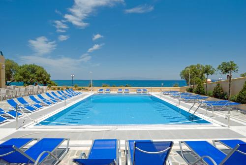 a swimming pool with chairs and the ocean in the background at Aegean Dream Hotel in Karfas