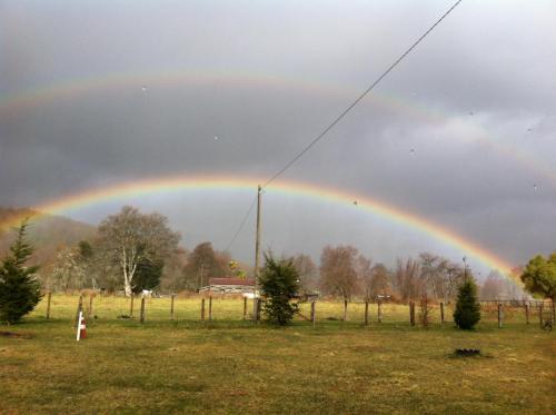 a rainbow in a field with a person standing in a field at Cabañas Captren Andino in Curacautín