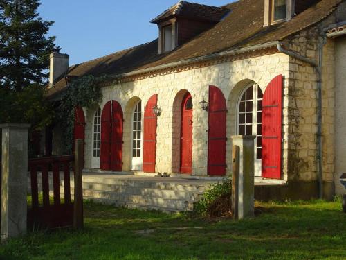 un antiguo edificio de ladrillo con puertas rojas y una valla en B&B Les Quatre Vents, en Montpon-Ménestérol