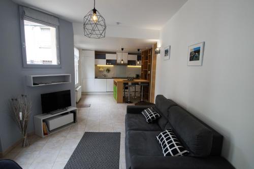 a living room with a black couch and a kitchen at La Petite Madame in Moret-sur-Loing