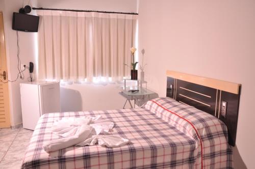 a bedroom with a bed with a plaid blanket and a table at Hotel Capim Dourado in Palmas