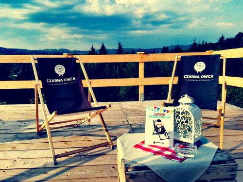 two chairs and a table with a book on a deck at Czarna Owca in Istebna