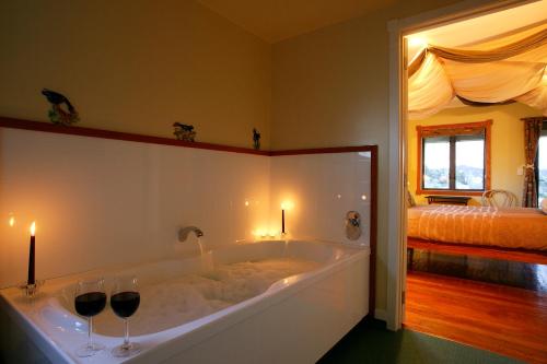 a bath tub with two wine glasses and a bed at Abseil Inn in Waitomo Caves