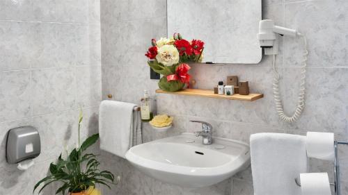 bagno con lavandino, specchio e fiori di Hotel Gamma a Milano