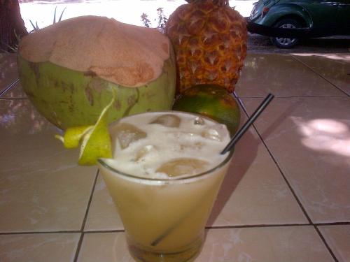 a drink sitting on a table with a avocado and a pineapple at Hostal Camping Beach in Salinas