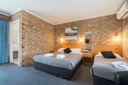 a bedroom with two beds and a brick wall at Citrus Valley Motel in Renmark