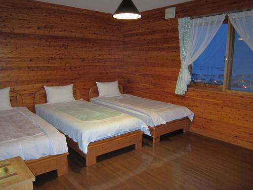 Pension Yamasan في Nakafurano: سريرين في غرفة خشبية مع نافذة