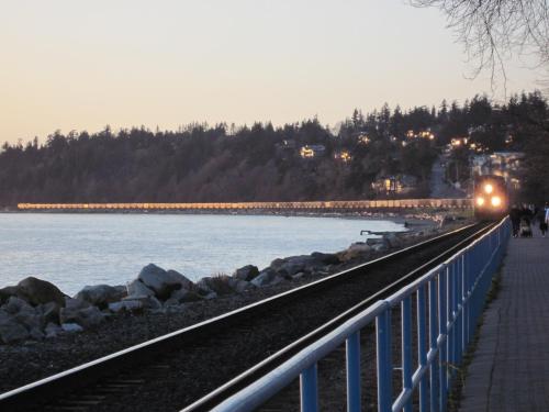 a train traveling down the tracks next to the water at Ocean Promenade Hotel in White Rock