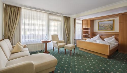 a hotel room with a bed and a couch and chairs at Hotel Schweizer Hof Thermal und Vital Resort in Bad Füssing