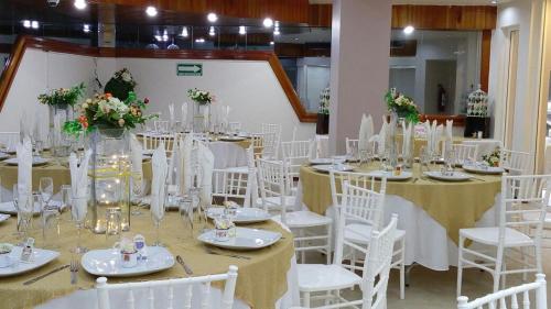 a room full of tables and chairs with white tables and white chairs at Hotel Cabildos in Tapachula