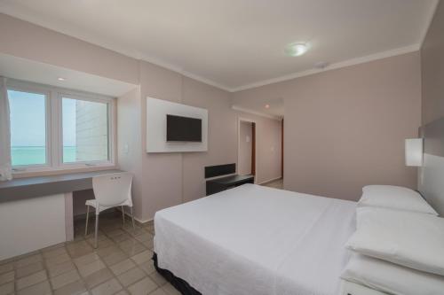 a bedroom with a bed and a desk and a window at Hotel Sete Coqueiros in Maceió