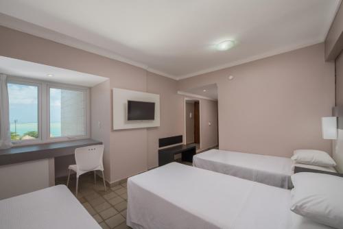 a bedroom with two beds and a desk and a tv at Hotel Sete Coqueiros in Maceió