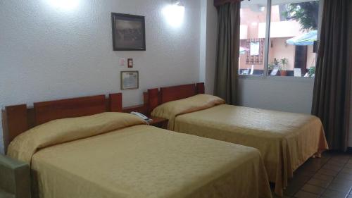 a hotel room with two beds and a window at Hotel Cabildos in Tapachula