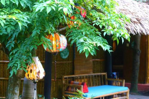 a tree with two lamps and a table and a bench at Under The Coconut Tree Hoi An Homestay in Hoi An