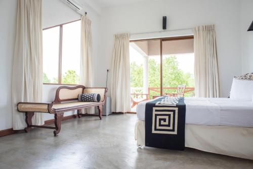 a bedroom with a bed and a chair and windows at Nagenahira Beach Villa in Nilaveli