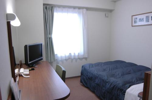 a bedroom with a bed and a desk with a television at Hotel Econo Tsu Station in Tsu