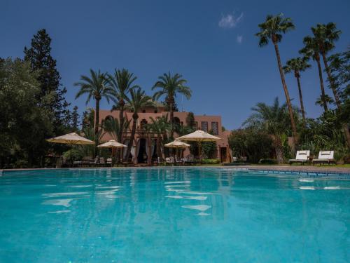 une grande piscine bordée de palmiers et un bâtiment dans l'établissement Dar Ayniwen Garden Hotel & Bird Zoo, à Marrakech