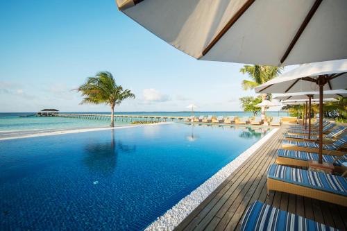 a swimming pool with chairs and umbrellas and the ocean at ROBINSON NOONU - All Inclusive in Manadhoo