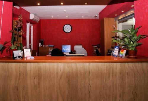 a reception desk with a clock on a red wall at Parrots Sitges Hotel in Sitges