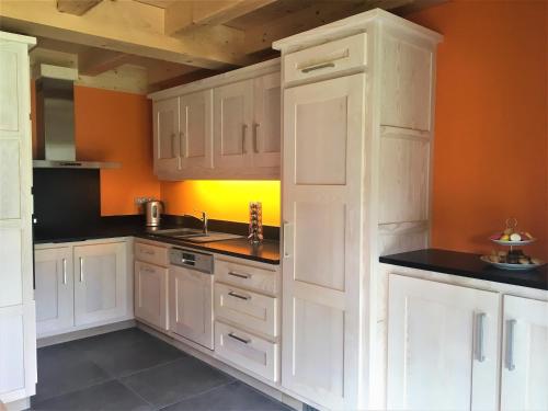 uma cozinha com armários brancos e uma parede laranja em Chalet Luxe Les Mélèzes em Samoëns