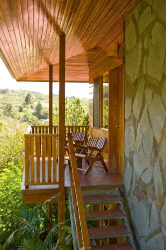 a wooden porch with two chairs and a stone wall at Arco Iris Lodge in Monteverde Costa Rica