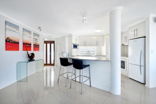 a kitchen with white cabinets and a bar with stools at ULTIQA Shearwater Resort in Caloundra