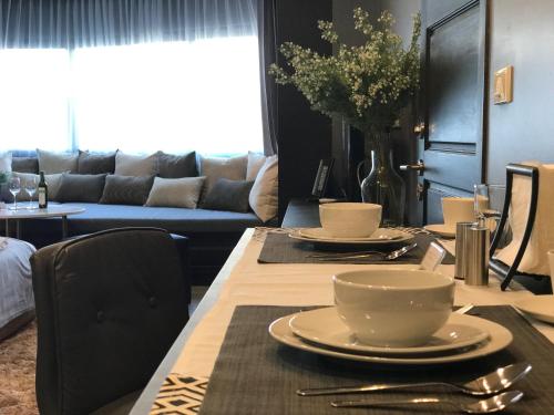 a dining room table with plates and cups and a couch at Stay in Style at Nimman R306B in Chiang Mai