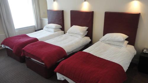 une chambre d'hôtel avec 3 lits et des couvertures rouges dans l'établissement Sandyford Hotel, à Glasgow