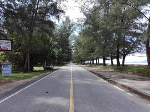 an empty road with trees on either side at Fisherman's Hut , ขนำชาวเลโฮมสเตย์ in Pak Meng