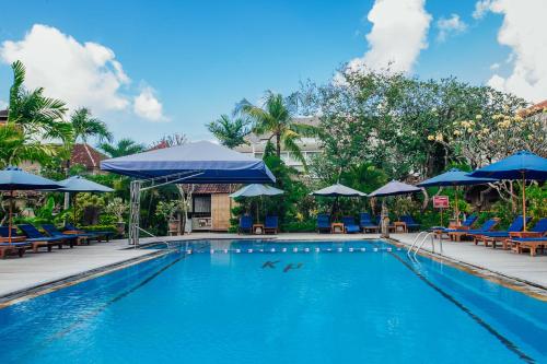a swimming pool with blue chairs and umbrellas at Kuta Puri Bungalows, Villas and Resort in Kuta