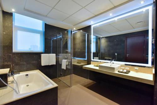 a bathroom with a tub and a sink and a mirror at Ramada by Wyndham Manama City Centre in Manama