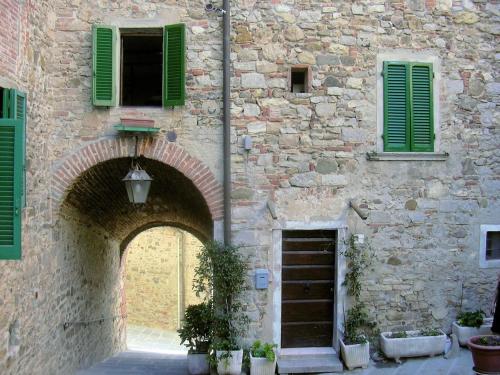 ルチニャーノにあるCasa Vacanza Lucignanoの緑の鎧戸とアーチ道のある石造りの建物