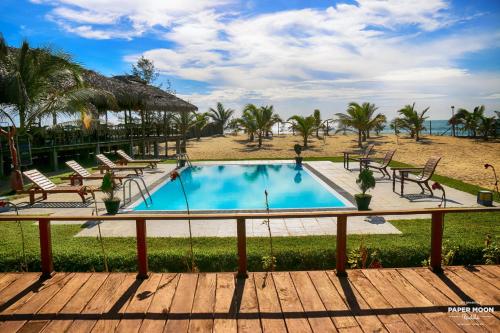 a swimming pool with chairs and the beach at Paper Moon Kudils in Arugam Bay