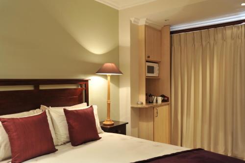 a bedroom with a bed with red pillows and a lamp at Claires of Sandton Luxury Guest House in Johannesburg