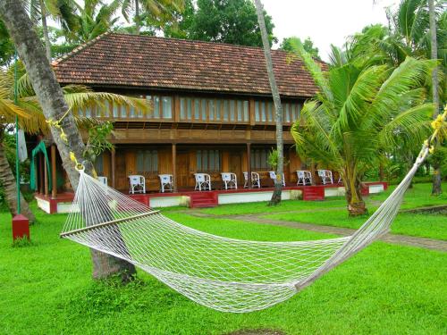 a hammock in front of a house with chairs at Coconut Lagoon Kumarakom - A CGH Earth Experience in Kumarakom